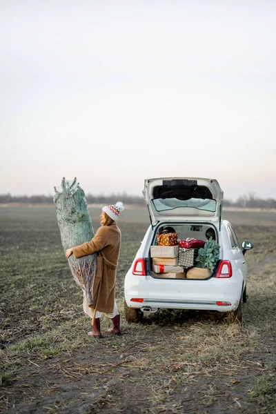 Kvinna går med julgran nära bilen på naturen — Stockfoto