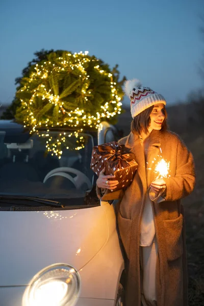 車の近くにスプリンクラーとクリスマスツリーを持つ女性屋外 — ストック写真