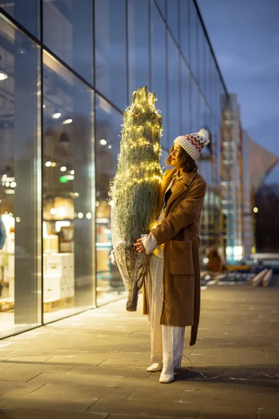 Femme portant un sapin de Noël illuminé près du centre commercial — Photo