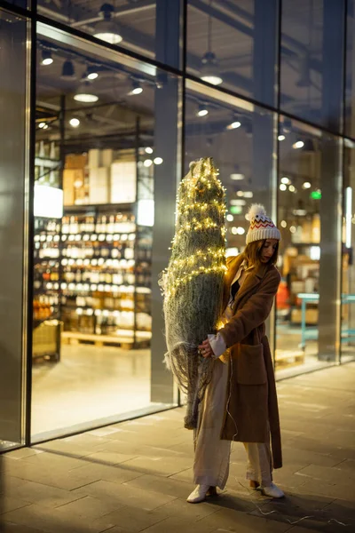 Woman carrying illuminated Christmas tree near the shopping centre — Stock Photo, Image