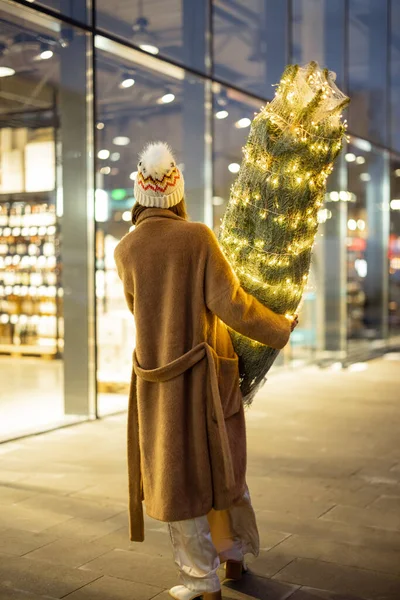 Mujer llevando árbol de Navidad iluminado cerca del centro comercial —  Fotos de Stock