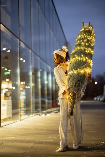 ショッピングセンターの近くにライトアップされたクリスマスツリーを持つ女性 — ストック写真