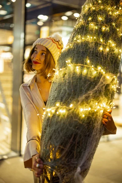 商场附近的妇女提着灯火辉煌的圣诞树 — 图库照片