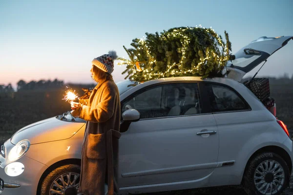 Mulher com sprklers perto de carro e árvore de Natal ao ar livre — Fotografia de Stock