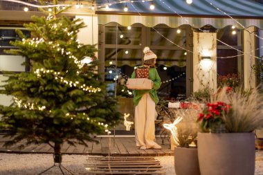 Yılbaşı süslenmiş arka bahçesinde hediyelerle yürüyen bir kadın.