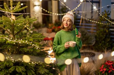 Yeni yıl dekore edilmiş arka bahçede elinde kurabiye ve fincanla bir kadın.