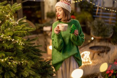 Yeni yıl dekore edilmiş arka bahçede elinde kurabiye ve fincanla bir kadın.