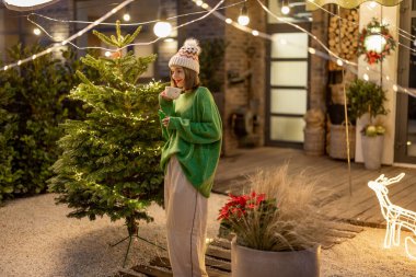 Yeni yıl dekore edilmiş arka bahçede elinde kurabiye ve fincanla bir kadın.