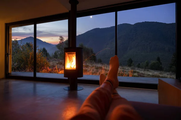 Donna che riposa vicino al camino in casa moderna con splendida vista sulle montagne al tramonto. — Foto Stock