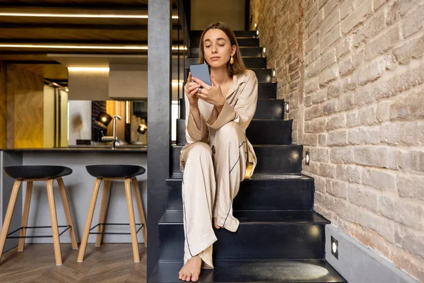 Kvinna som använder telefon sittande på trappor i modern lägenhet — Stockfoto