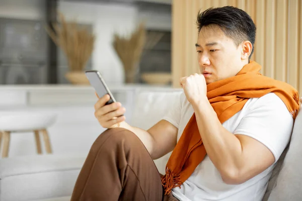 Hasta Asyalı adam öksürüyor ve akıllı telefon kullanıyor. — Stok fotoğraf