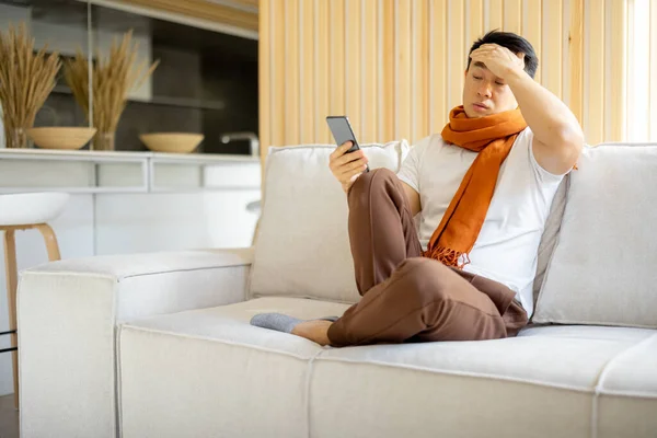 Zieke aziatische man hoesten en met behulp van smartphone — Stockfoto