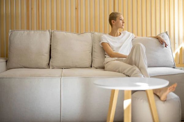 Woman sit and rest on sofa at home — kuvapankkivalokuva