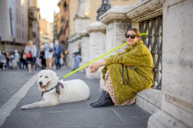 Beyaz köpekli bir kadın Roma 'da sokakta oturuyor.