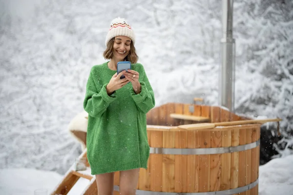Frau mit Handy ruht sich mit heißem Bad in verschneiter Natur aus — Stockfoto