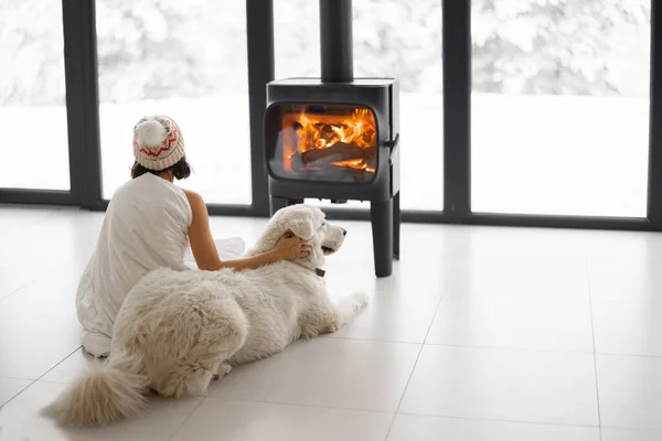 Žena se psem doma s hořícím krbem během zimy — Stock fotografie