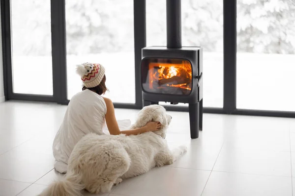 Mulher com cão em casa com lareira em chamas durante o inverno — Fotografia de Stock