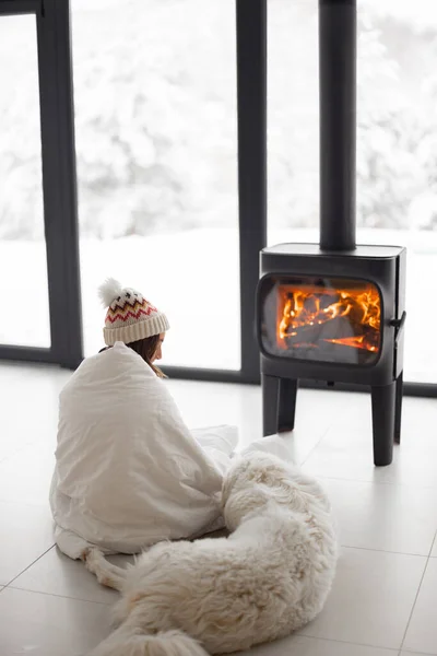 Woman with dog at home with burning fireplace during wintertime — Stock Photo, Image