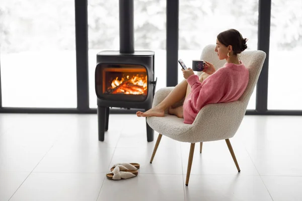 自然の家で暖炉のそばで椅子にカップを持つ女性 — ストック写真