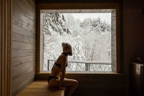 Mulher descansando na sauna com vista sobre a natureza nevada — Fotografia de Stock