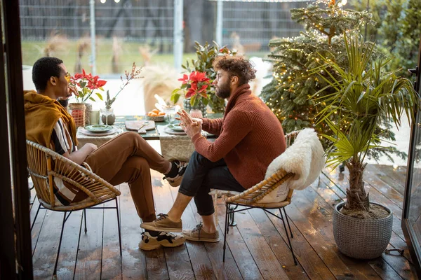 Två manliga flerrasvänner som har ett nära samtal och sitter vid ett middagsbord på bakgården — Stockfoto