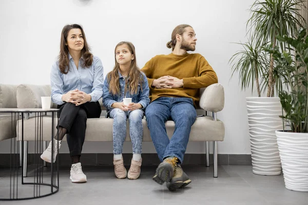Família com uma menina sentada em um sofá na sala de espera da clínica — Fotografia de Stock