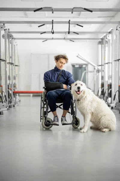 Tipo con discapacidad en silla de ruedas con su perro de asistencia en el centro de rehabilitación —  Fotos de Stock