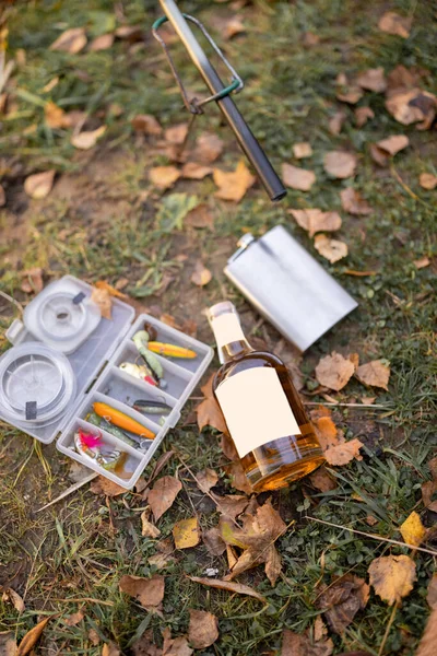 装有酒精饮料的酒瓶，放在有钓具的草地上 — 图库照片