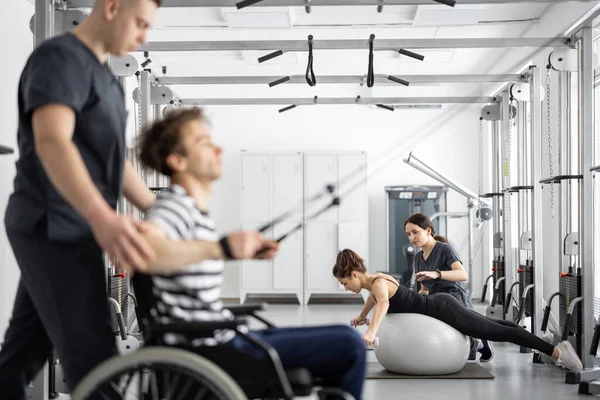 Especialista en rehabilitación ayuda a un chico en silla de ruedas a hacer ejercicio — Foto de Stock