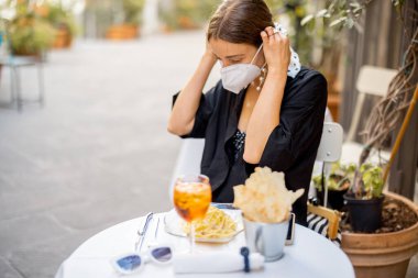 Kadın İtalyan restoranında otururken maskesini çıkarıyor.