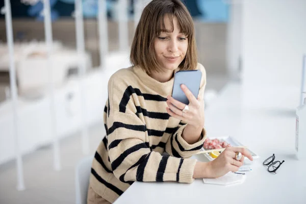 Молодая женщина использует телефон, сидя в ресторане — стоковое фото