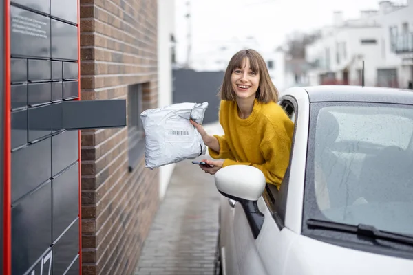 Žena vytahuje balík z poštovního terminálu přímo z okna auta na cestách — Stock fotografie