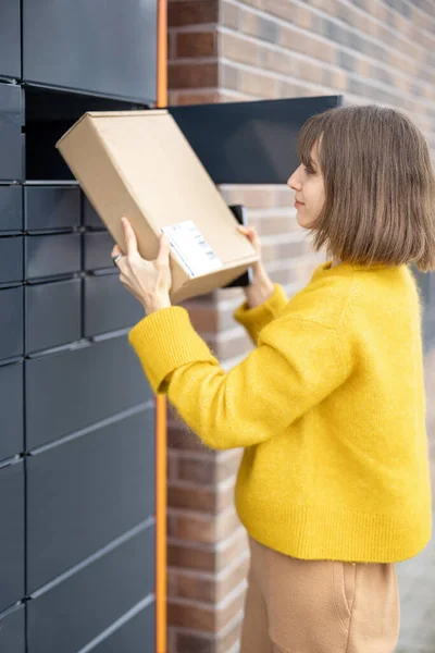 Жінка отримує посилку з комірки автоматичного поштового терміналу на відкритому повітрі — стокове фото