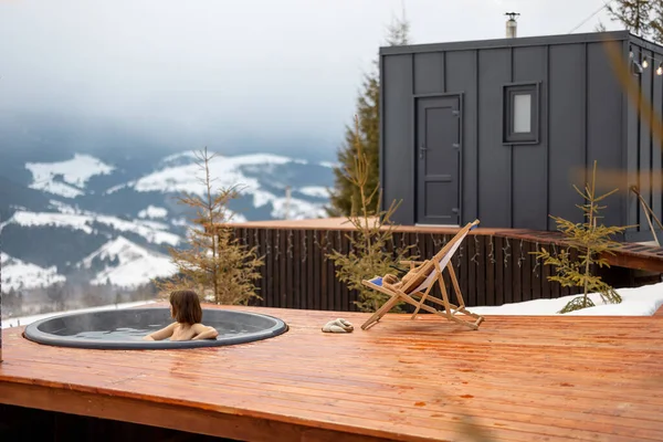 Mujer nada en baño caliente mientras descansa en una pequeña casa moderna en las montañas — Foto de Stock