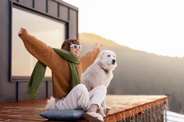 Žena se svým psem odpočívá na terase malého domku na přírodě — Stock fotografie