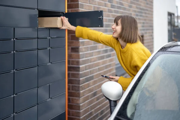 Žena vytahuje balík z poštovního terminálu přímo z okna auta na cestách — Stock fotografie