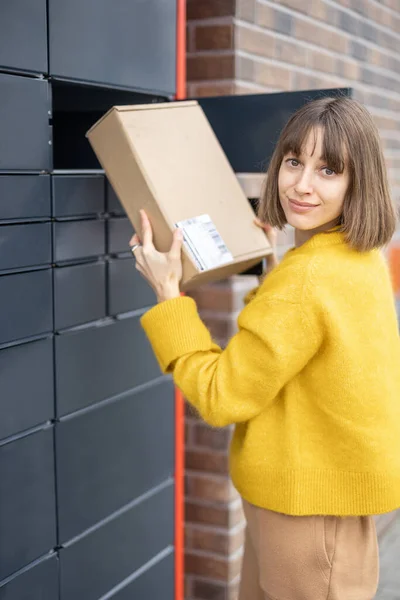 Жінка отримує посилку з комірки автоматичного поштового терміналу на відкритому повітрі — стокове фото
