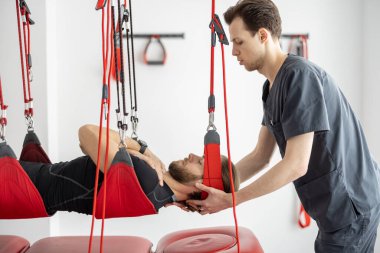 Rehabilitasyon uzmanı erkek hastaya süspansiyon kayışları üzerinde aktif tedavi uyguluyor.