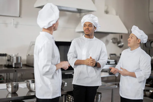 Drie multiraciale koks praten terwijl ze samen staan tijdens een pauze in de keuken van het restaurant — Stockfoto
