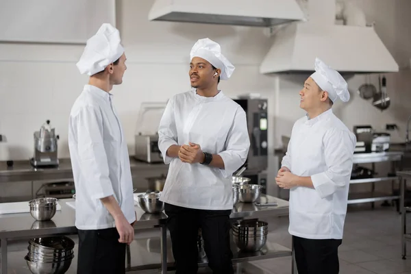 Três cozinheiros multirraciais conversam enquanto estão juntos durante uma pausa na cozinha do restaurante — Fotografia de Stock