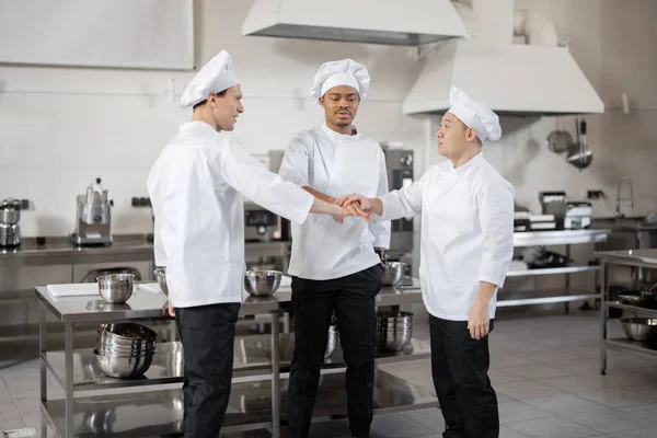 Equipe multirracial de chefs tomando as mãos juntos antes de um trabalho na cozinha — Fotografia de Stock