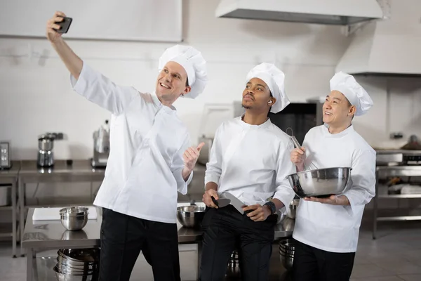 Drie multiraciale chef-koks nemen selfie foto op telefoon in restaurant keuken — Stockfoto