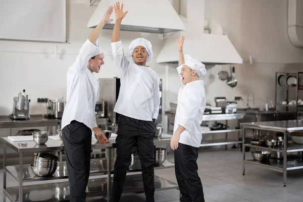 Equipo multirracial de chefs tomándose de la mano antes de un trabajo en la cocina — Foto de Stock