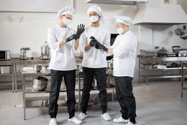 Team van chef-koks met beschermende handschoenen en gezichtsmaskers, voorbereiding op een baan in de keuken van het restaurant — Stockfoto