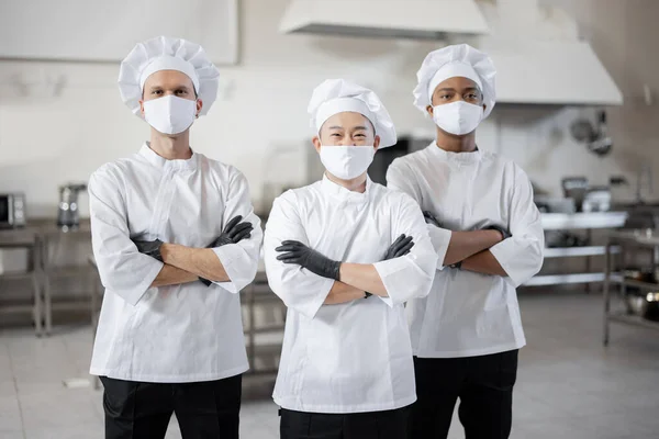 Drie goed geklede koks staan samen in de professionele keuken — Stockfoto