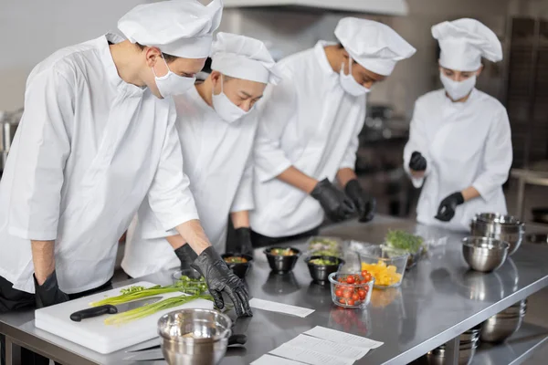 Equipo multirracial de cocineros mezclando ingredientes para llevar comida en cocina profesional —  Fotos de Stock