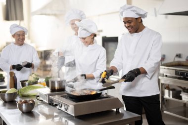 Üniformalı profesyonellerden oluşan çok ırklı bir ekip mutfaktaki bir restorana yemek hazırlıyor.