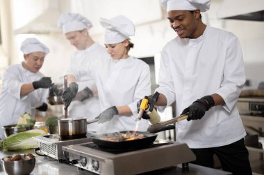 Üniformalı profesyonellerden oluşan çok ırklı bir ekip mutfaktaki bir restorana yemek hazırlıyor.