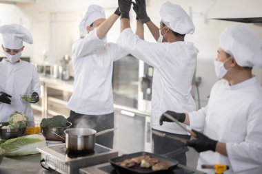 Aşçılardan oluşan çok ırklı bir ekip, profesyonel mutfakta yemek pişirirken el ele verip beşini birleştiriyor.
