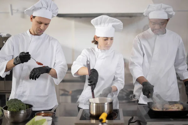 Equipe multirracial de três cozinheiros cozinhar na cozinha profissional — Fotografia de Stock